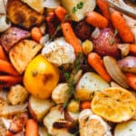 Roasted root vegetables with herbs, lemon and garlic in dish with serving spoon.