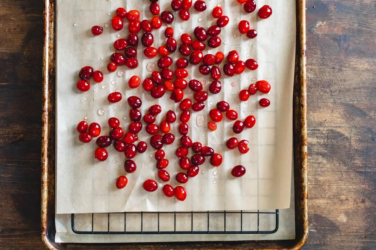 Whole cranberries soaked in sugar water on a baking sheet.