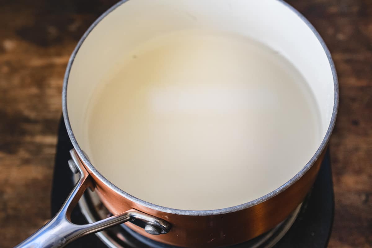 A sauce pan with sugar and water being dissolved on a burner. 