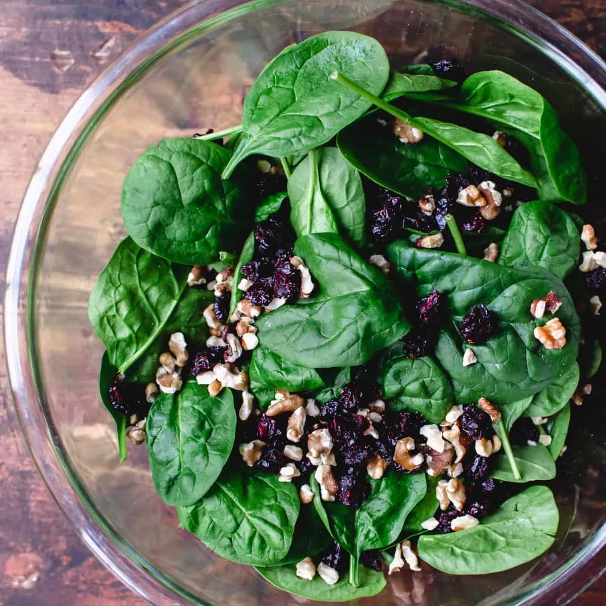Fresh baby spinach leaves, chopped walnuts and cranberries in glass bowl.