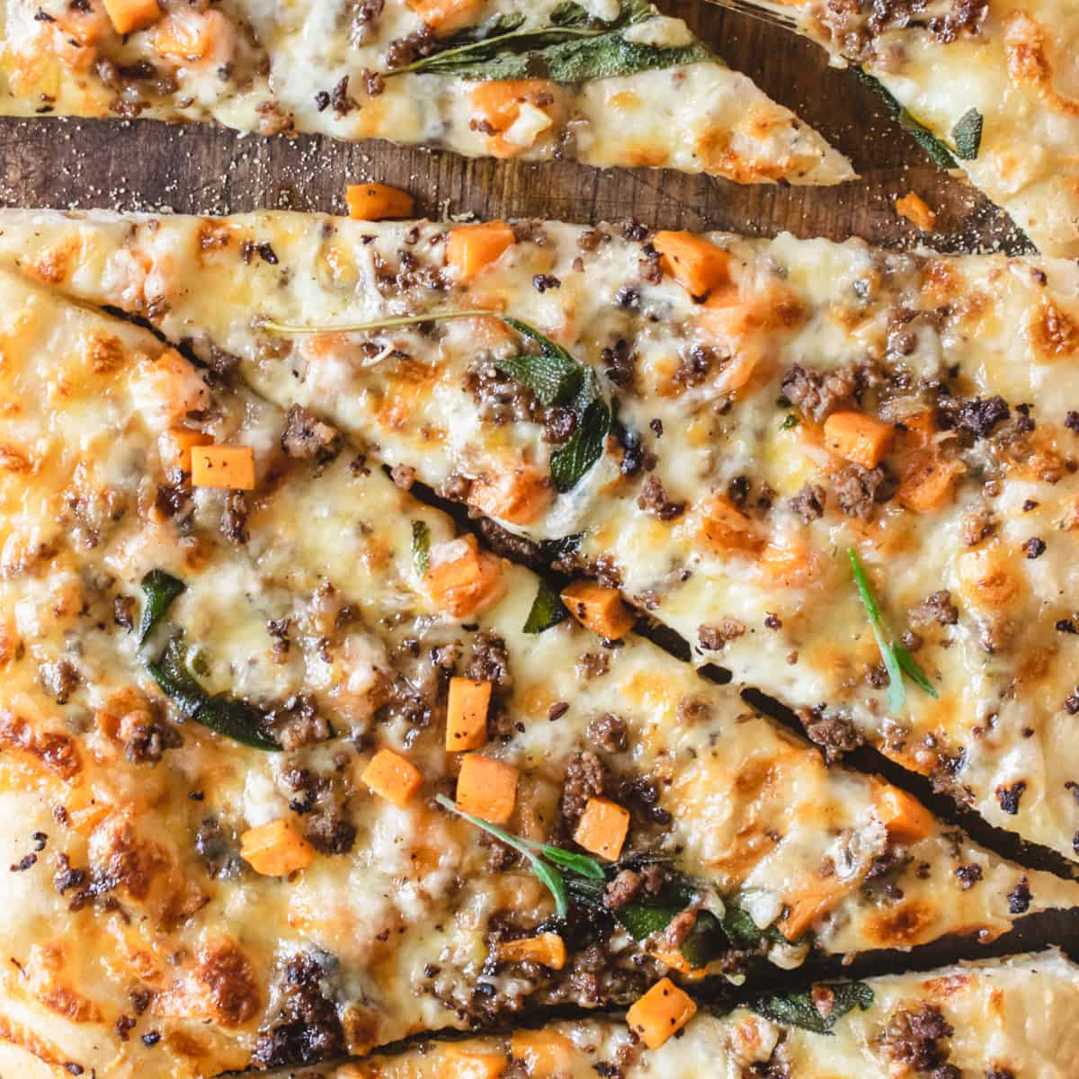 Pizza with cheese, sausage, sweet potato and sage on top.