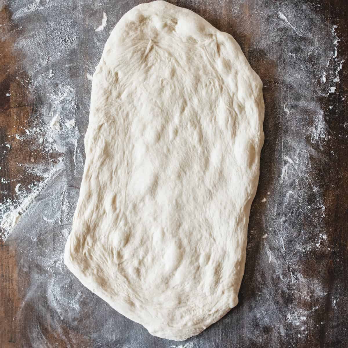 Rolled out pizza dough on a floured wooden cutting board