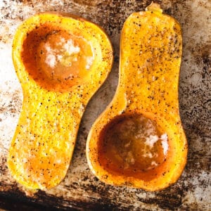 Roasted butternut squash on a baking sheet with salt and pepper.