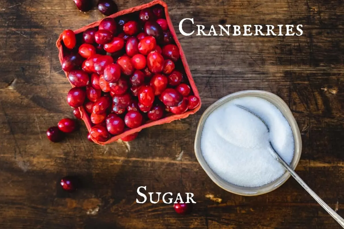 Fresh cranberries in a red fruit box by a bowl of sugar with a spoon.