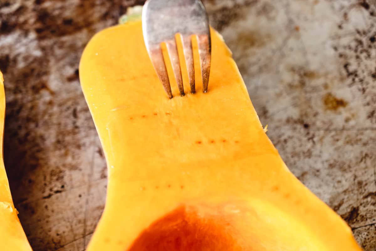 A fork poking holes in to a cut butternut squash.