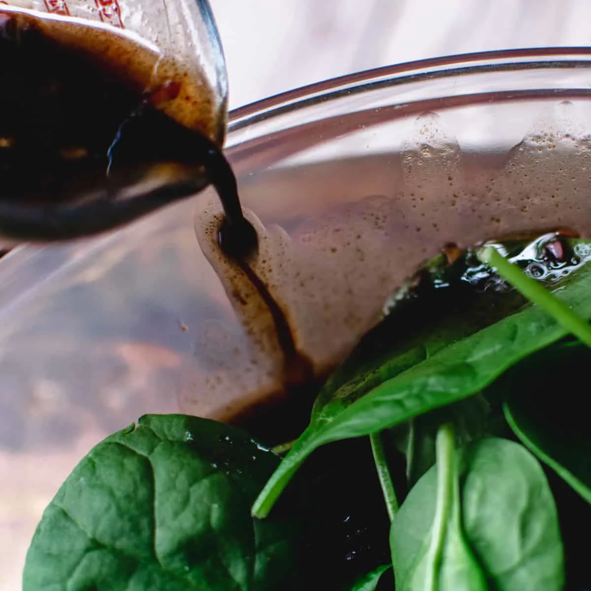 Balsamic salad dressing pouring onto edge of glass salad bowl.