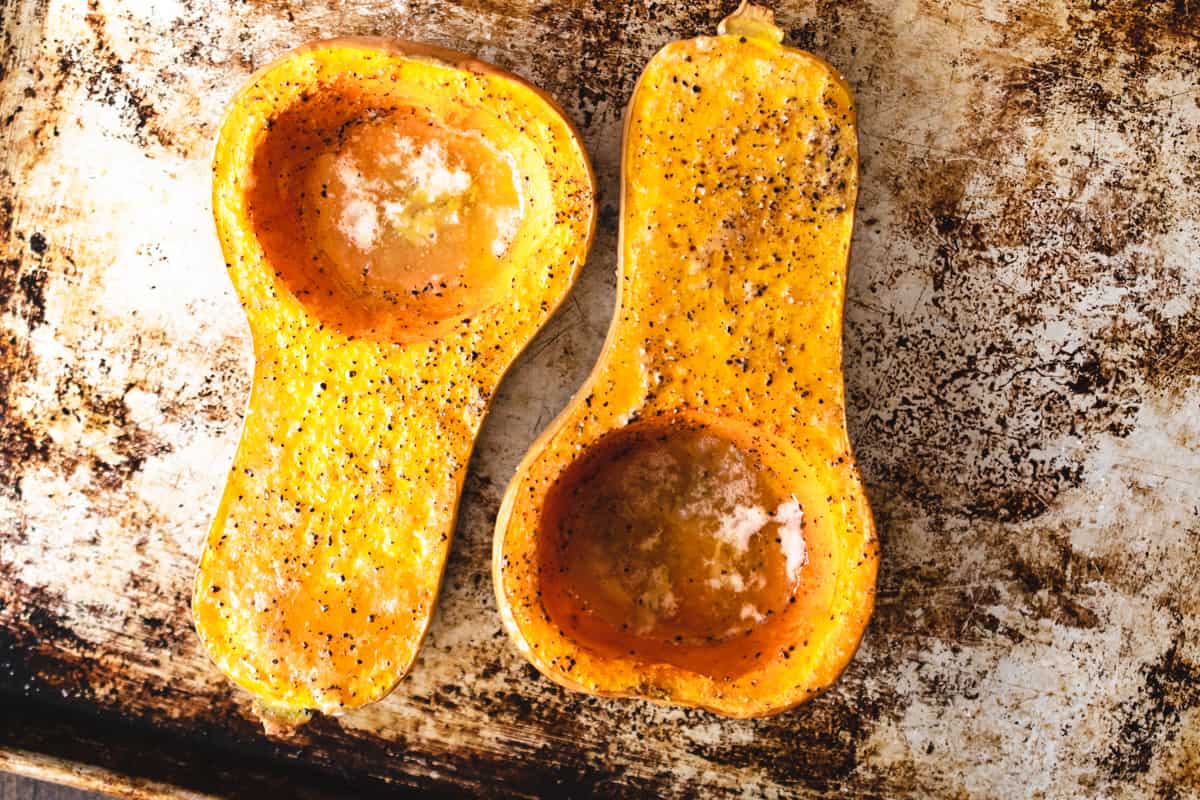 Roasted butternut squash on a baking sheet with salt and pepper.