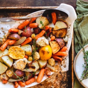 Roasted root vegetables in a baking dish with large serving spoon.