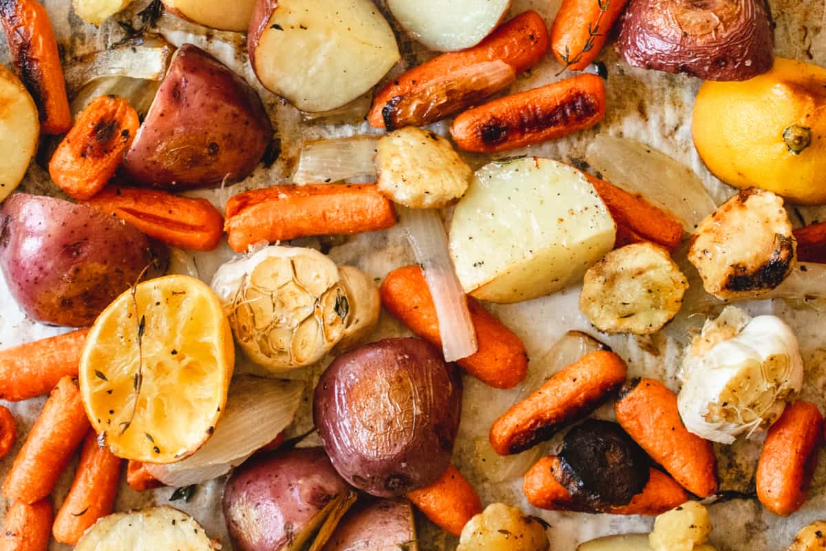 Roasted carrots, potatoes, garlic and parsnips on a baking sheet.
