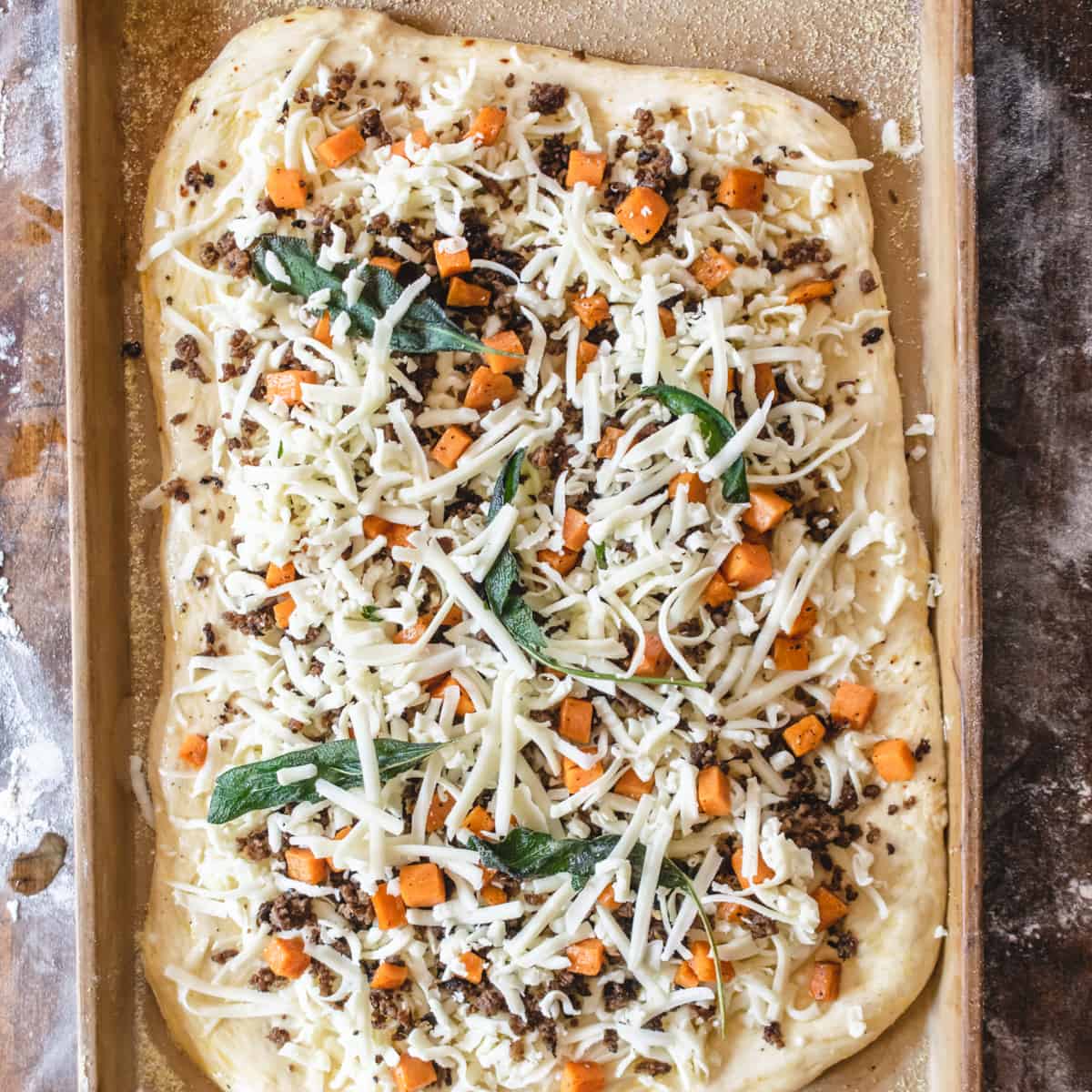 Uncooked pizza with Fall vegetables, cheese and herbs