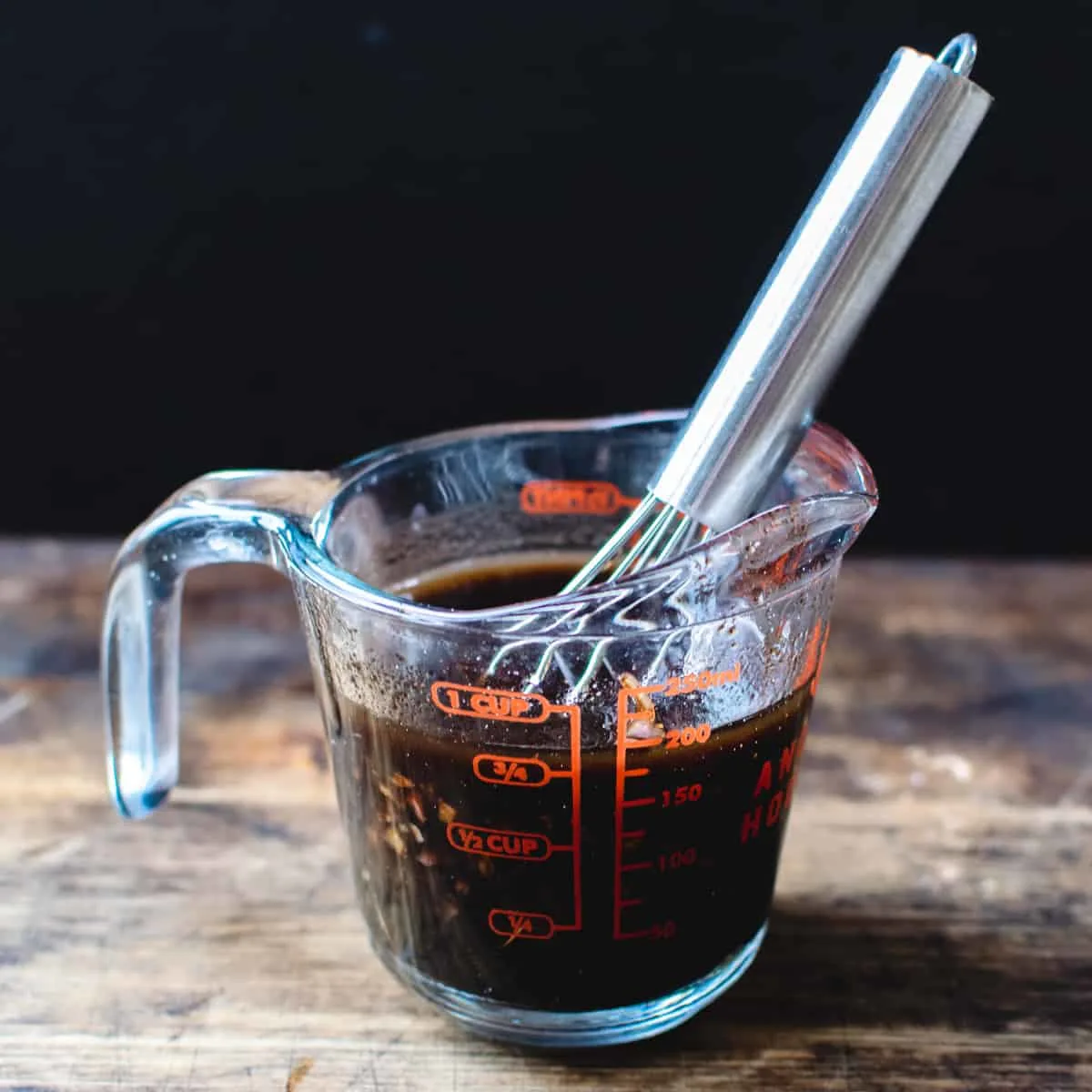 Balsamic vinegar, oil, shallot in a mixing cup with a metal whisk.