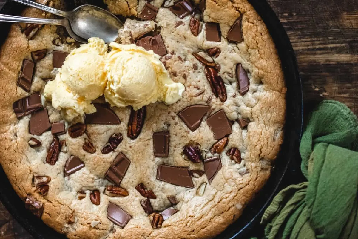 Cookie in a cast iron skillet with chunks of chocolate and pecans. 