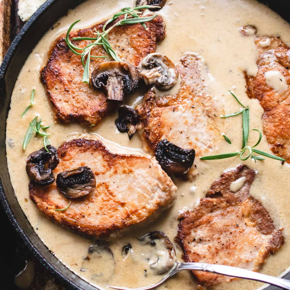 Boneless pork chops in mushroom gravy with rosemary and a spoon.