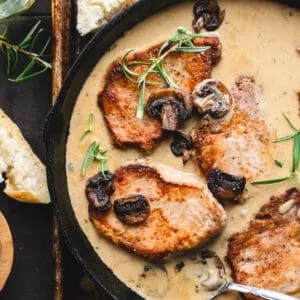Pork chops in an iron skillet with mushrooms, sauce and herbs.