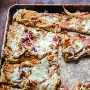 Crust topped with chicken, bacon, red onion and melted cheese and sliced into wedges on a baking sheet.
