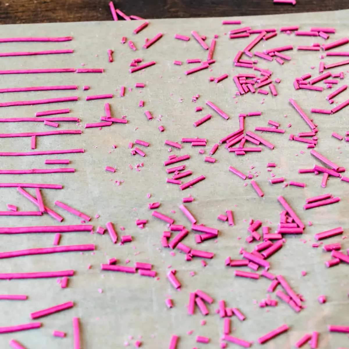 Piped lines of dried out pink sprinkle mixture being cut into small lines.