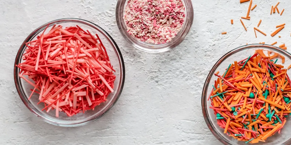 Multiple small bowls filled with multicolored and multi shaped sprinkles.