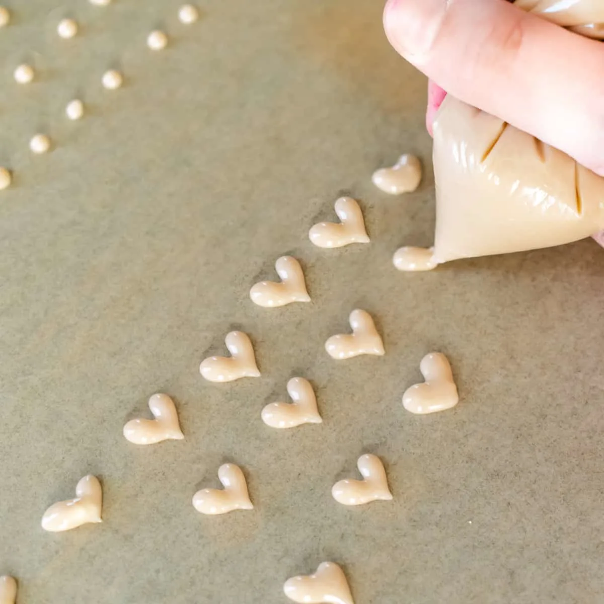 Piping heart shapes and dots onto brown parchment paper with pink sugar mixture.