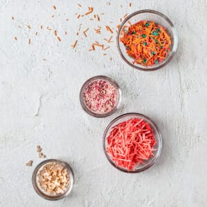 Several glass bowls filled with different shaped, sized and colored sprinkles on white background.