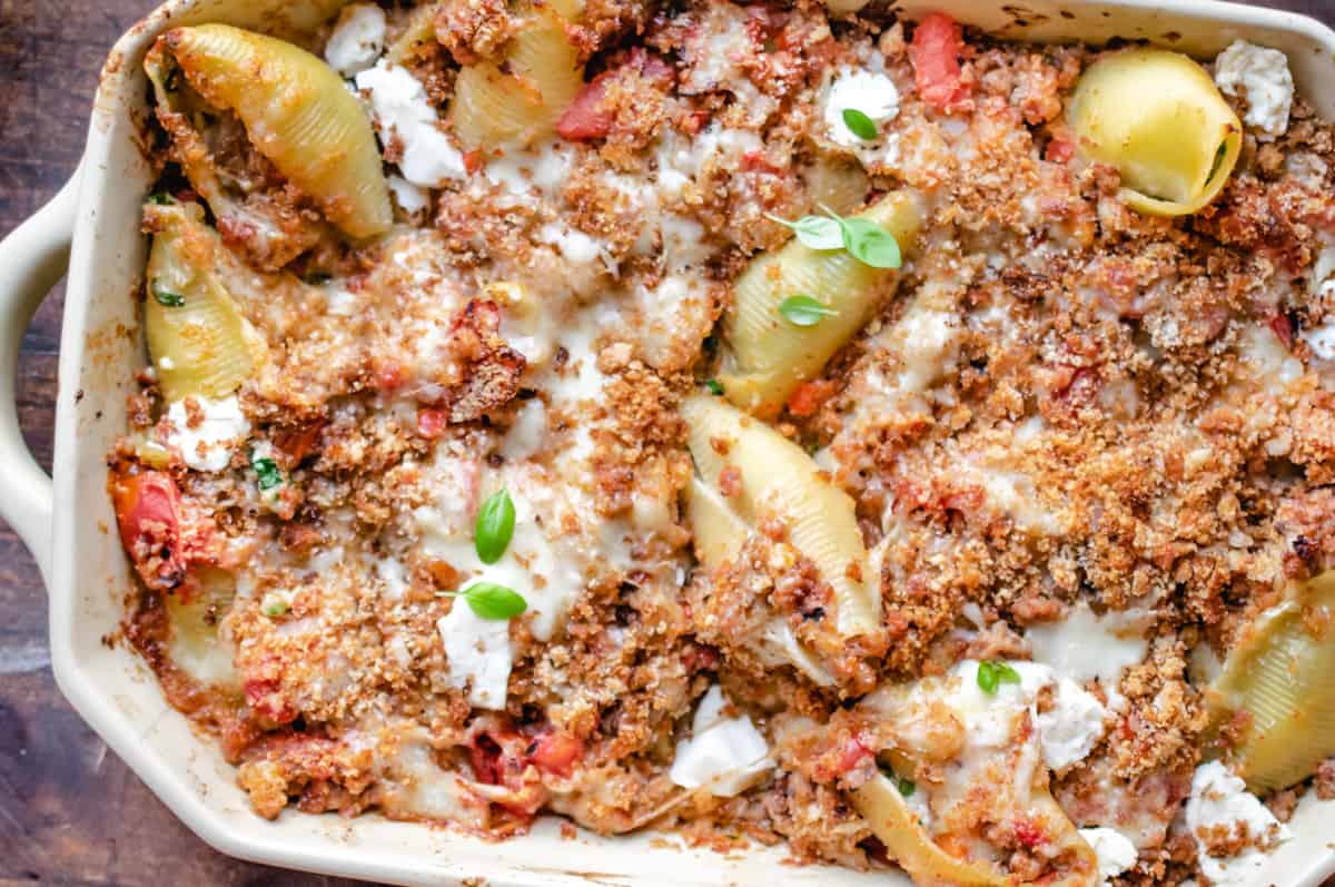 Rectangular casserole dish filled with pasta shells, cheese, fresh basil and breadcrumbs.