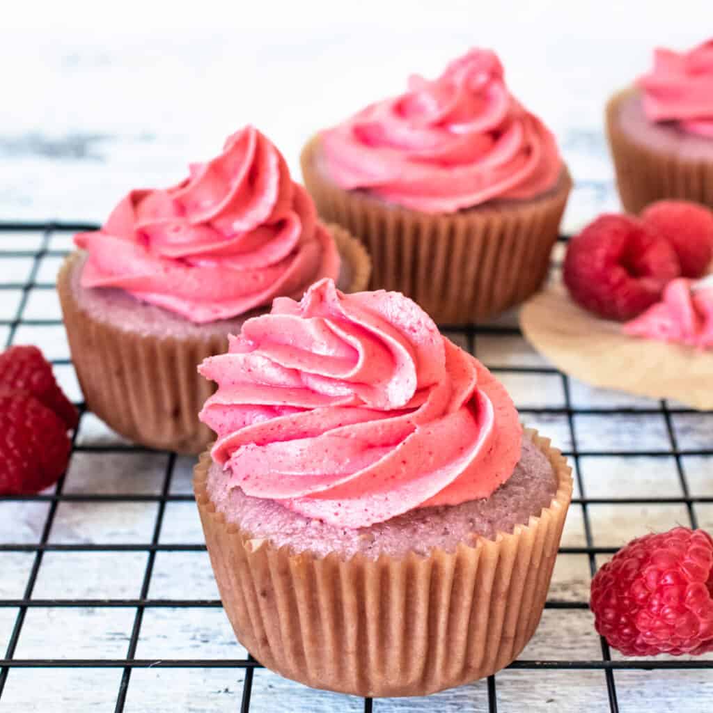 Pink raspberry cupcakes with frosting and fresh raspberries.