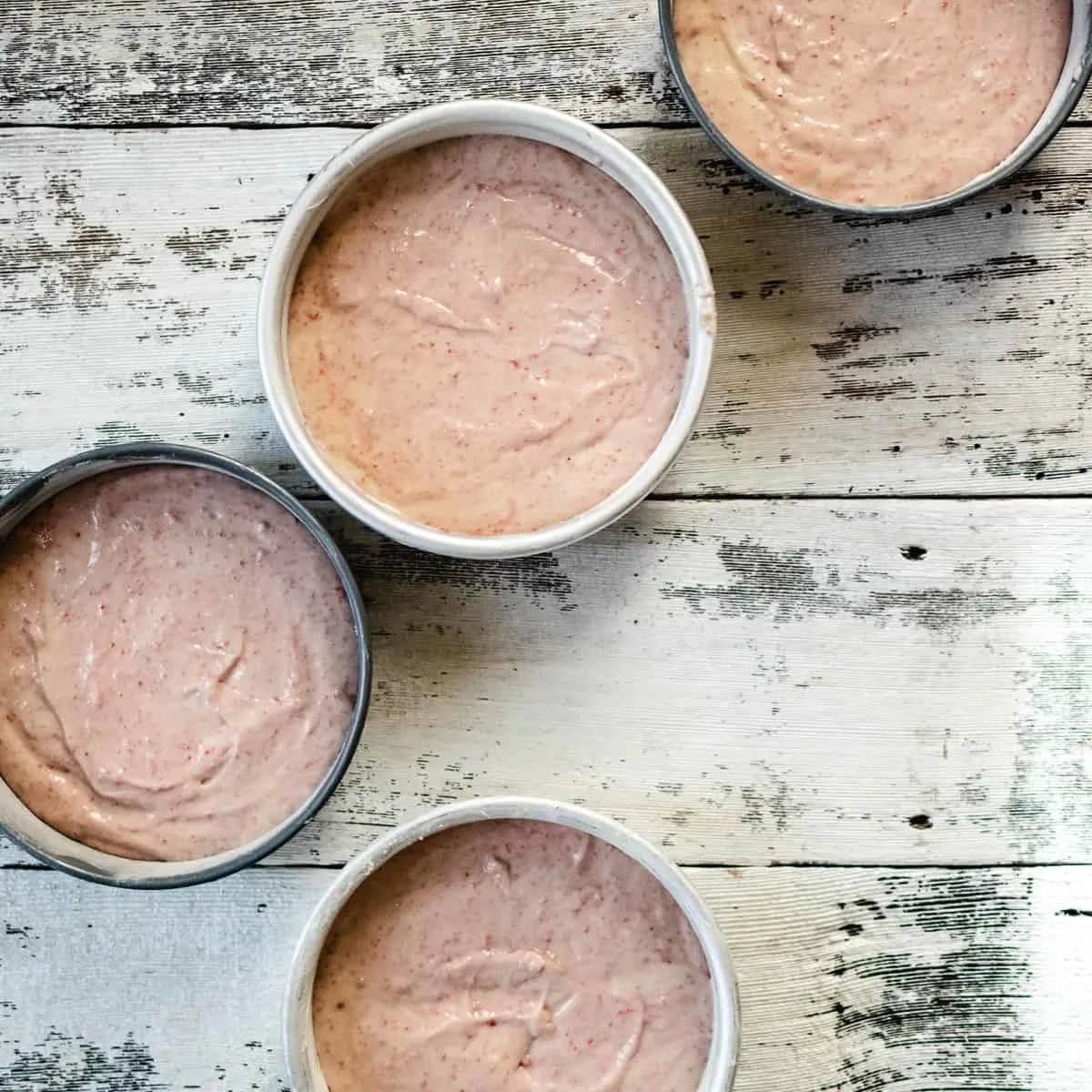 Four six inch cake pans filled with strawberry cake batter. 