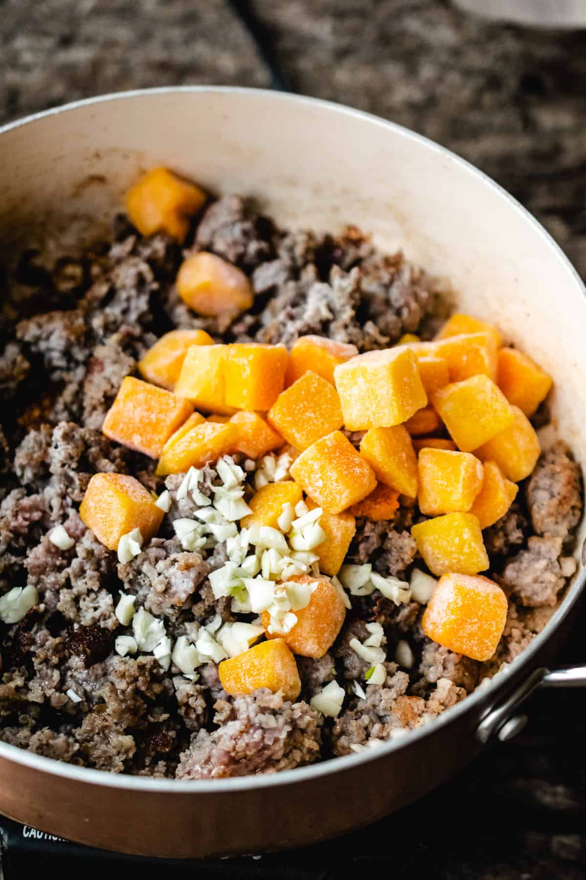 Ground Italian sausage, diced squash, and garlic sautéing in a copper skillet.