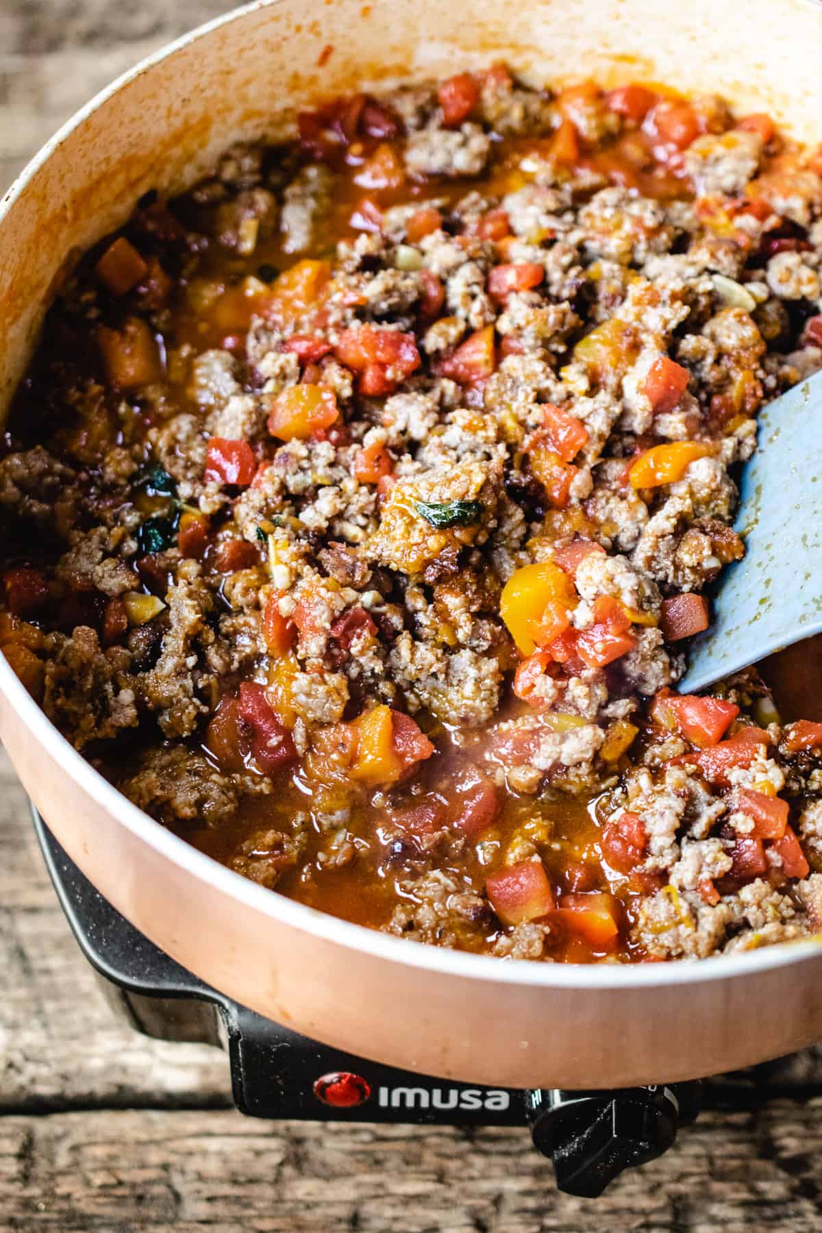 Ground sausage, tomatoes and herbs sautéing in a skillet.