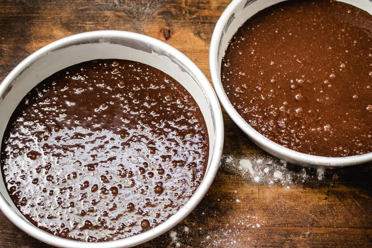 Chocolate cake batter poured into two round cake pans.
