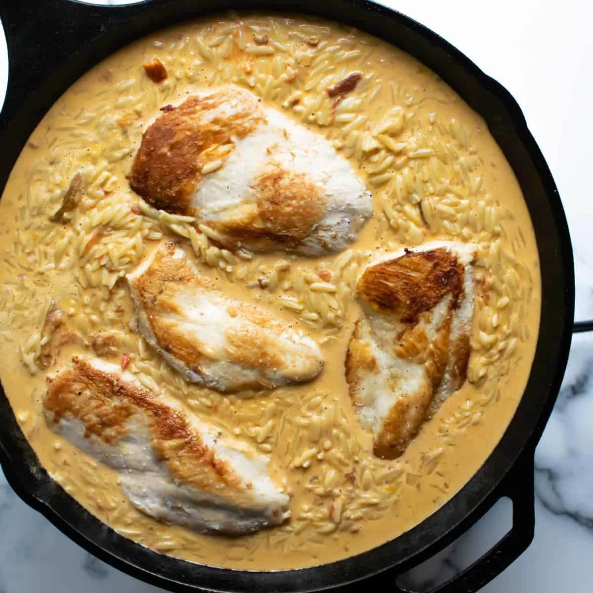 Chicken breasts and orzo cooking in a light sauce in a skillet.