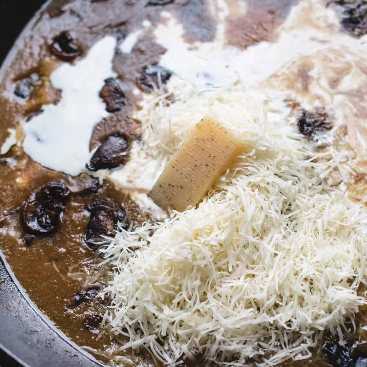 Cream and Parmesan cheese added to a mushroom soup base in a skillet. 