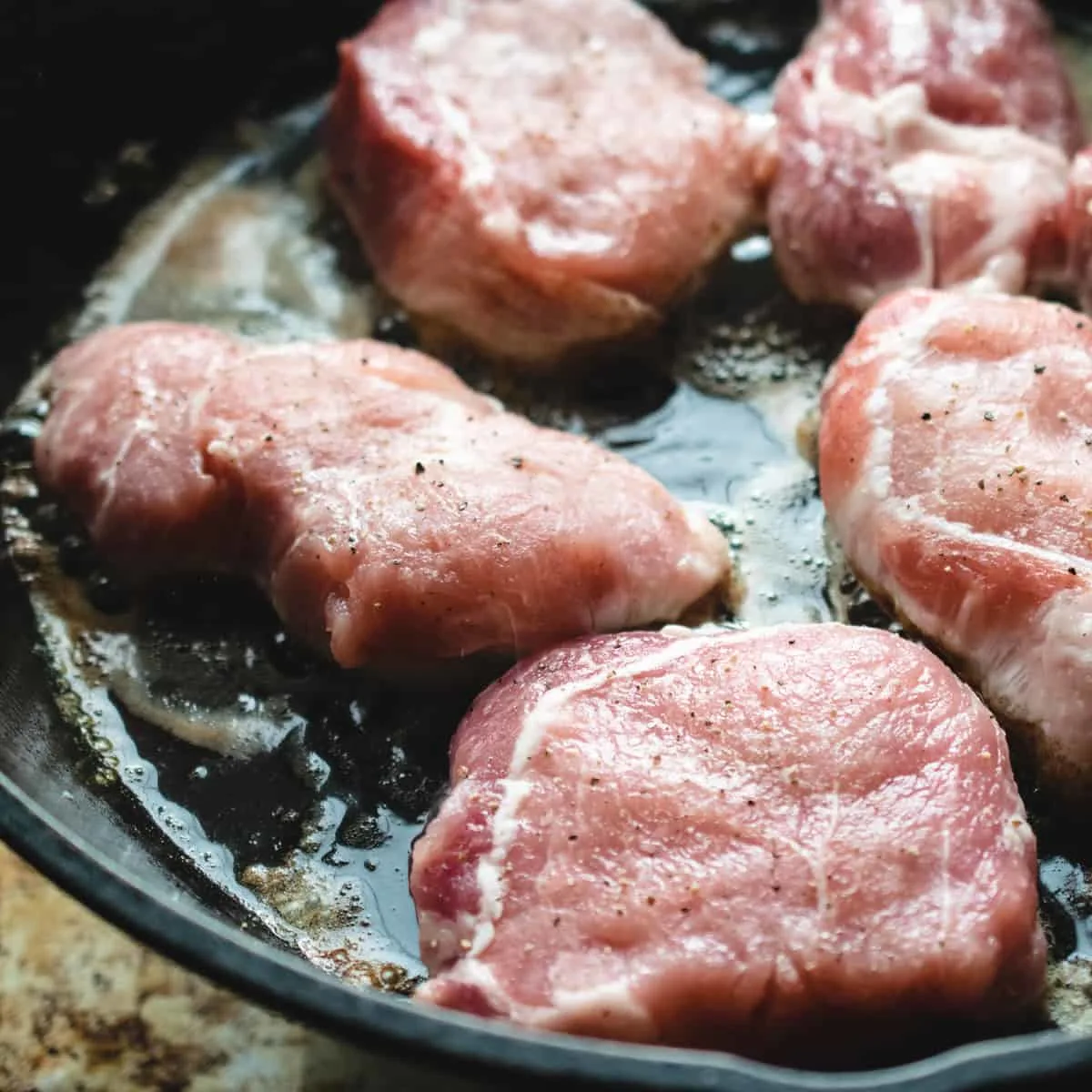 Pork chops searing in a hot skillet. 