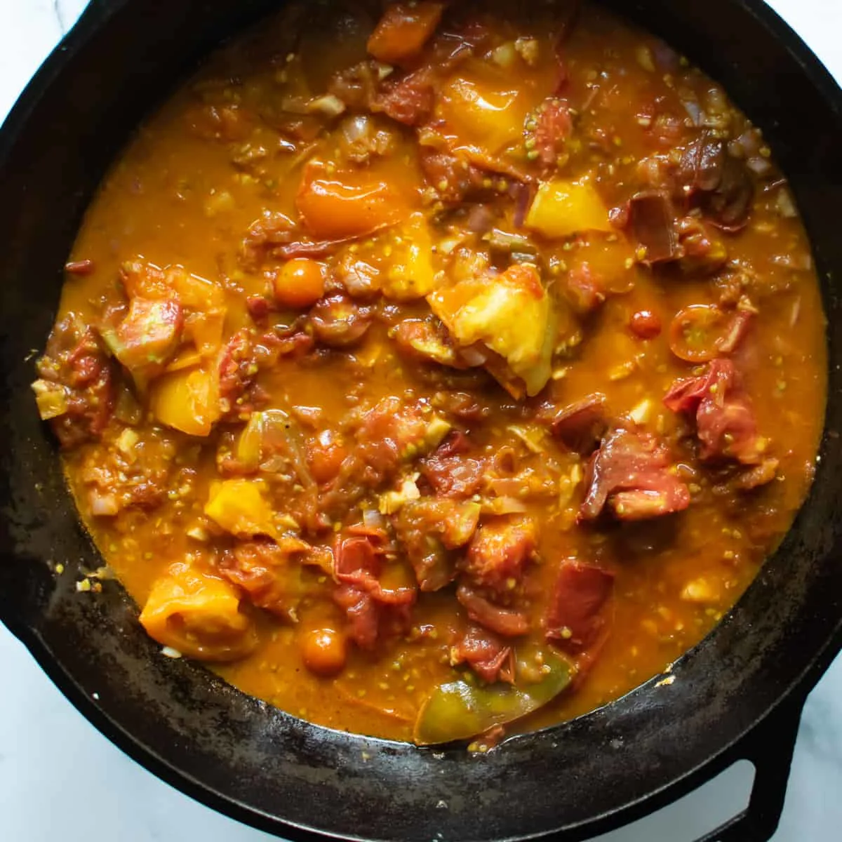 Sautéed tomatoes simmering in chicken stock in a skillet. 