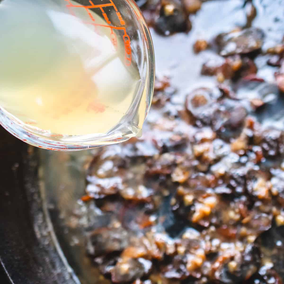 Pouring stock into a skillet of roux with minced shallot and garlic. 