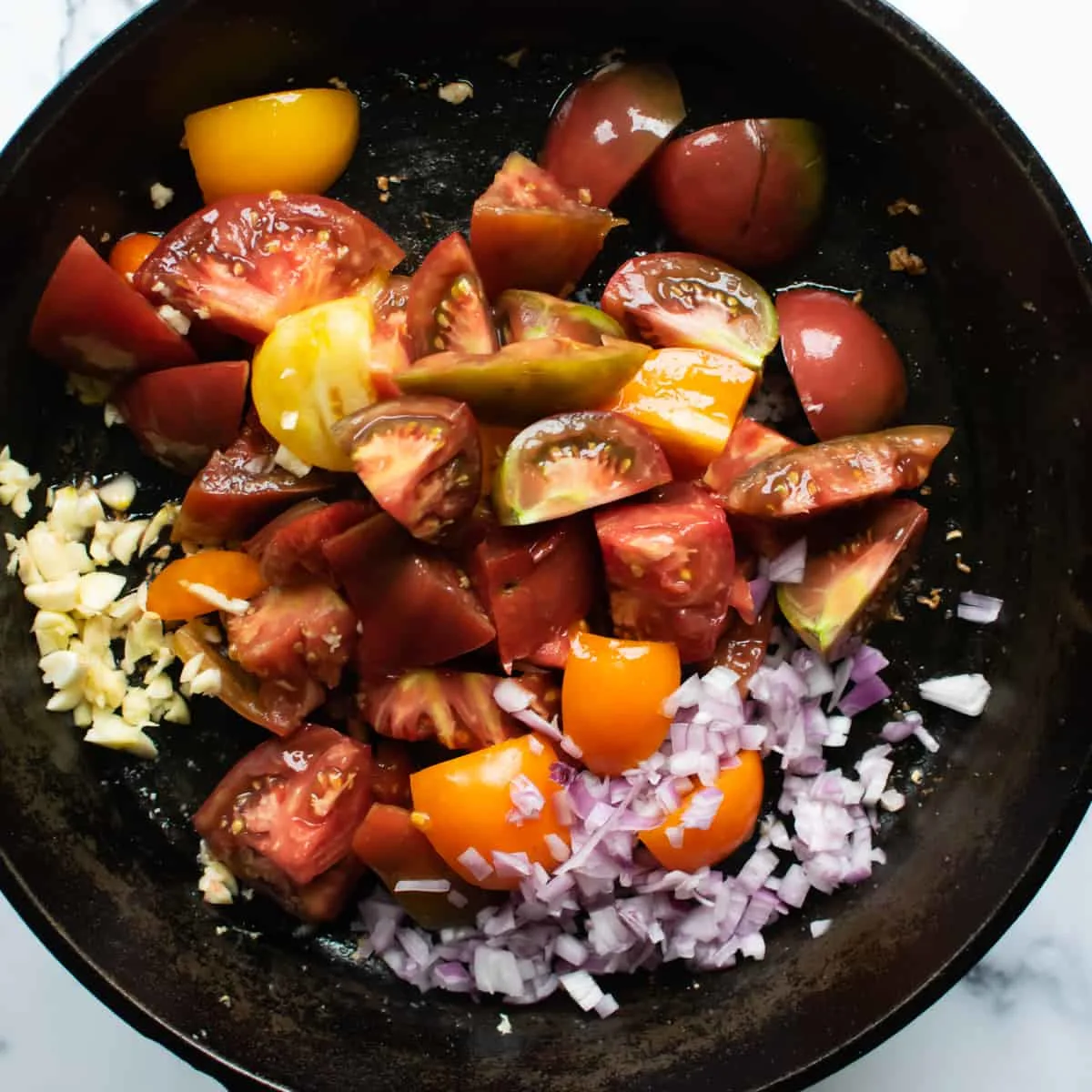 Sliced yellow, orange and red tomatoes with minced shallot and garlic in a skillet. 