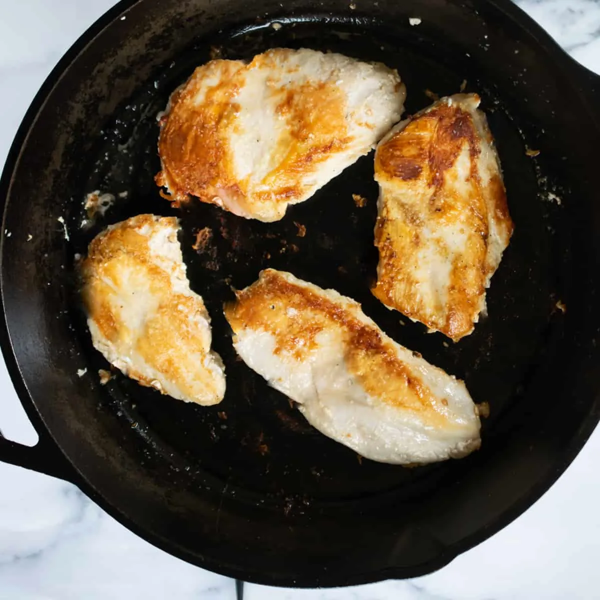 Four chicken breasts searing in a skillet. 