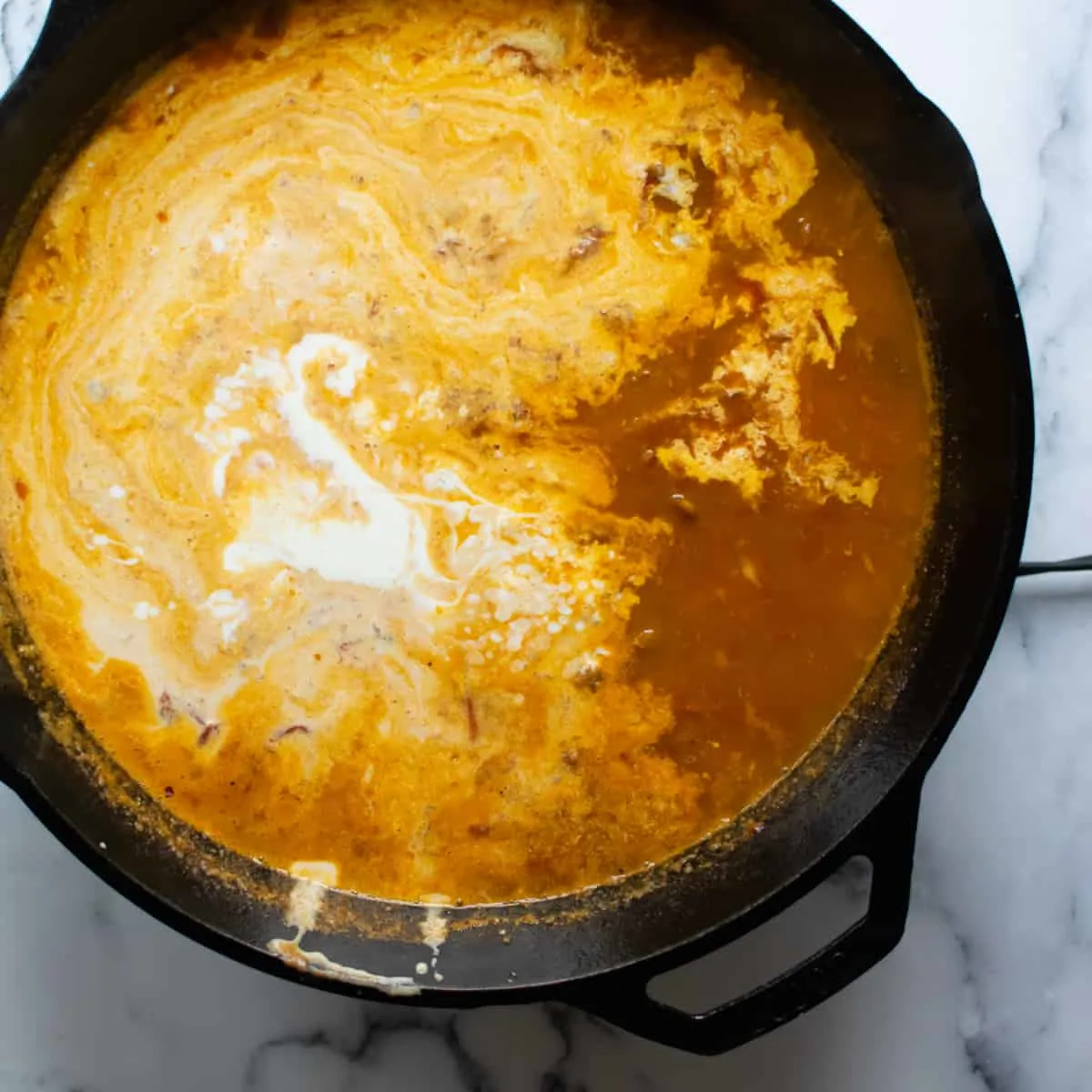 Cream stirred into a light tomato and chicken broth in a skillet.