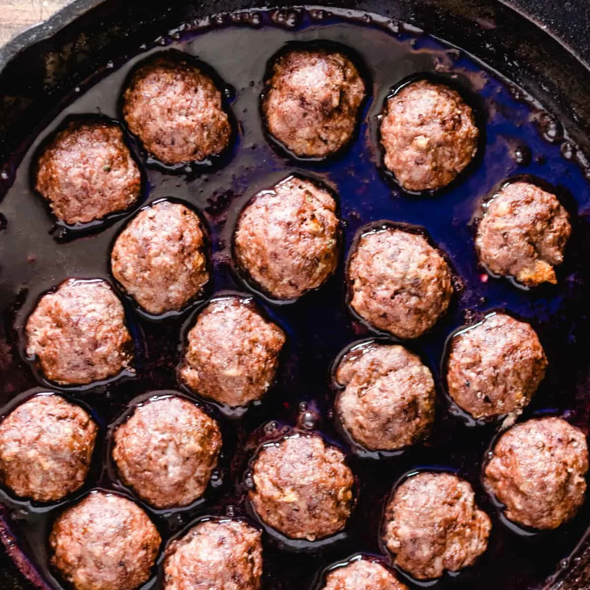 Meatballs simmering in a sauce in a skillet.
