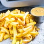 Crispy French fries in front of an air fryer with salt.