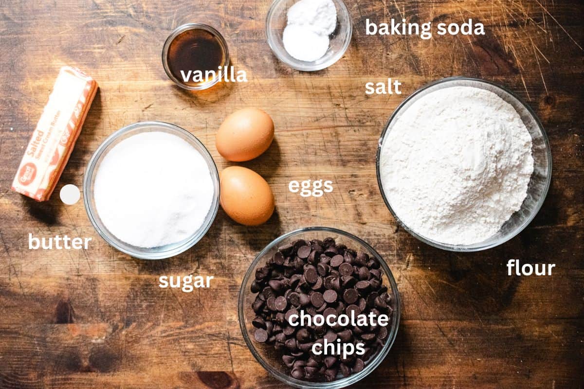 Butter, vanilla, sugar, eggs, baking powder, salt, flour and chocolate chips on a cutting board.