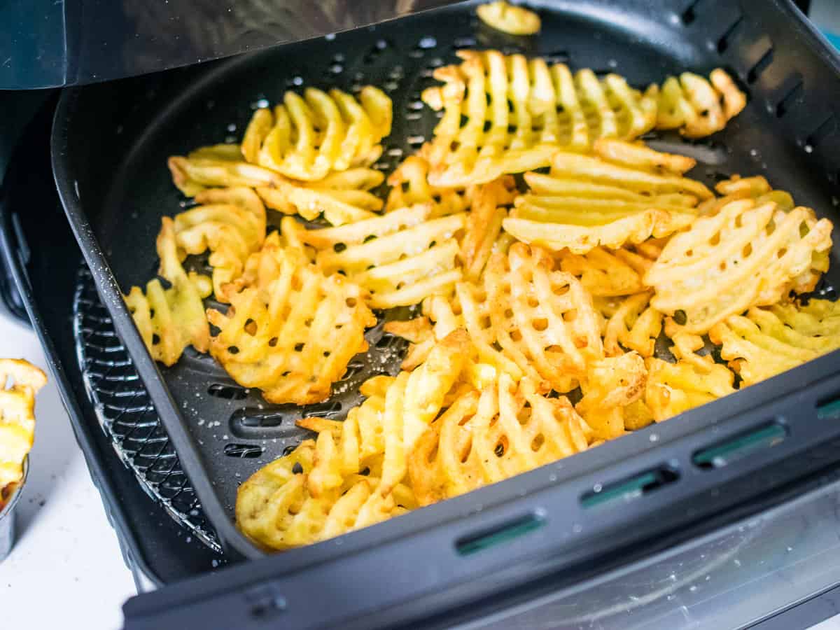 An air fryer basket filled with crisped waffle fries.