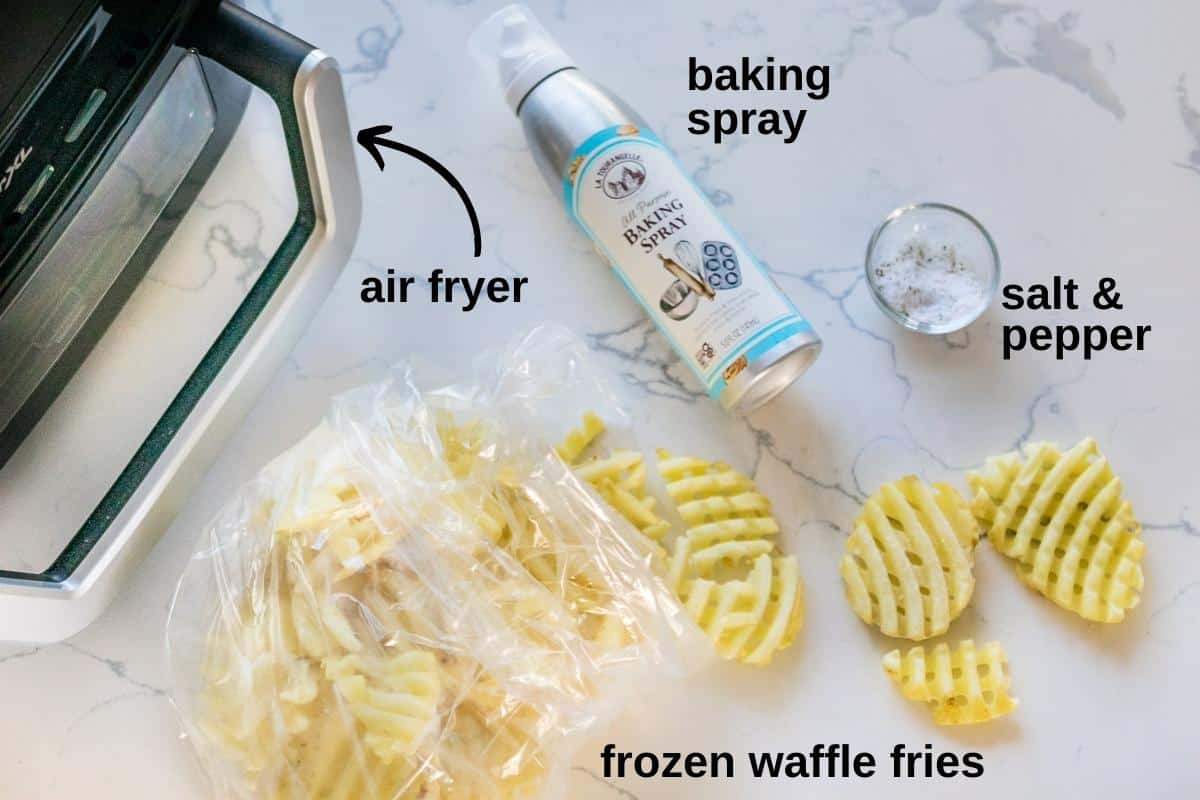An air fryer, baking spray, frozen waffle fries and salt on a counter.