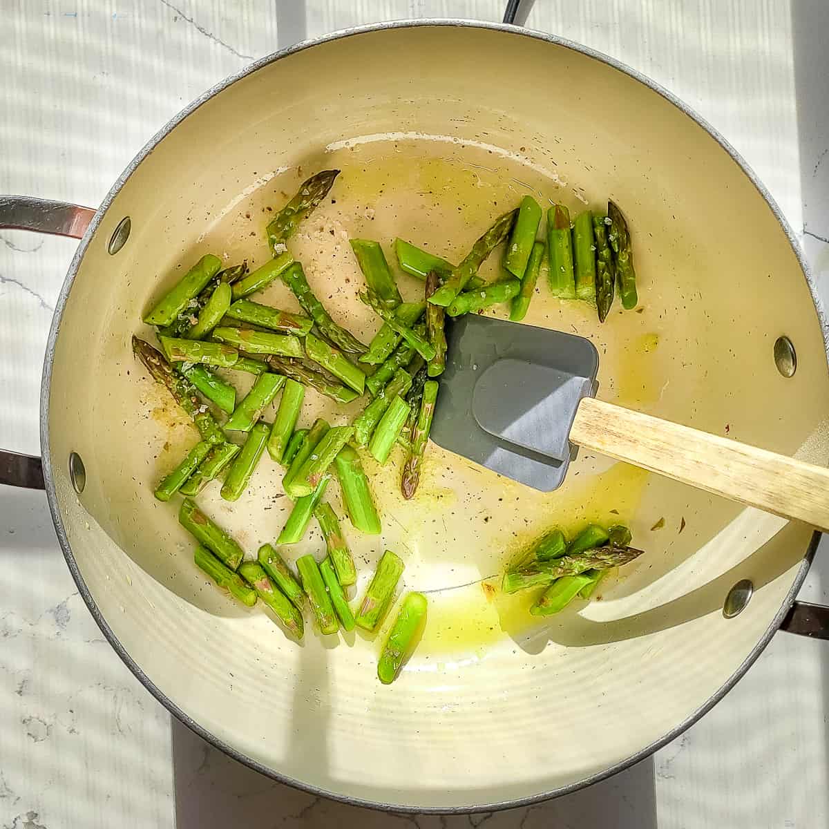 A pot of cut asparagus being sautéed in olive oil. 