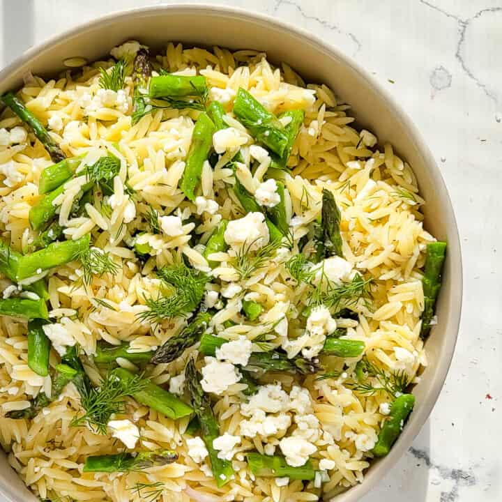 A bowl of chilled orzo pasta salad with asparagus and feta cheese.