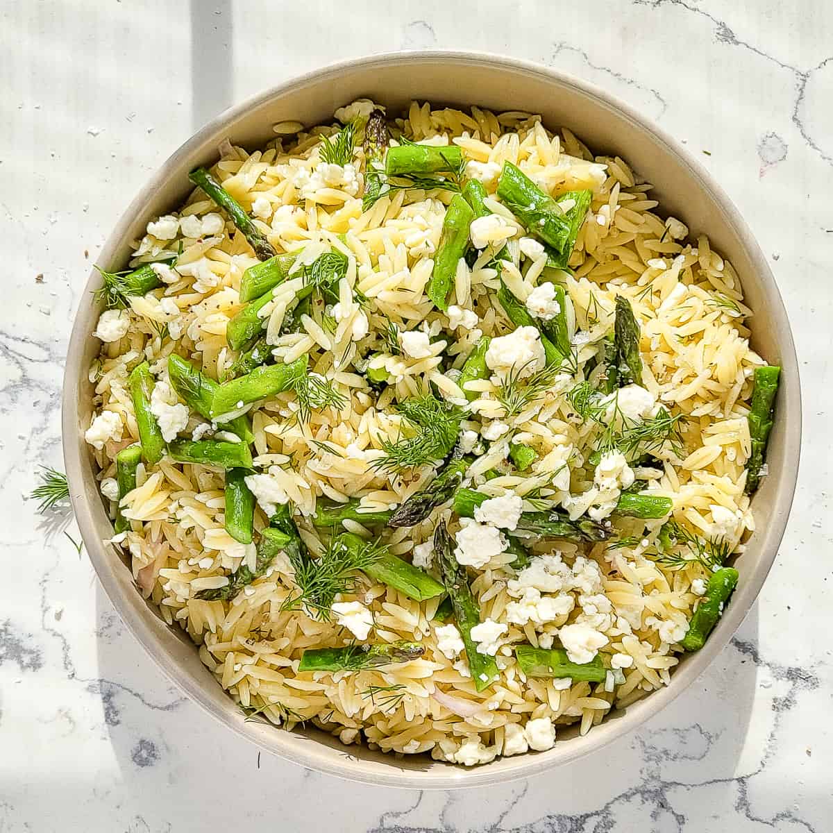 A bowl of chilled orzo pasta salad with asparagus.