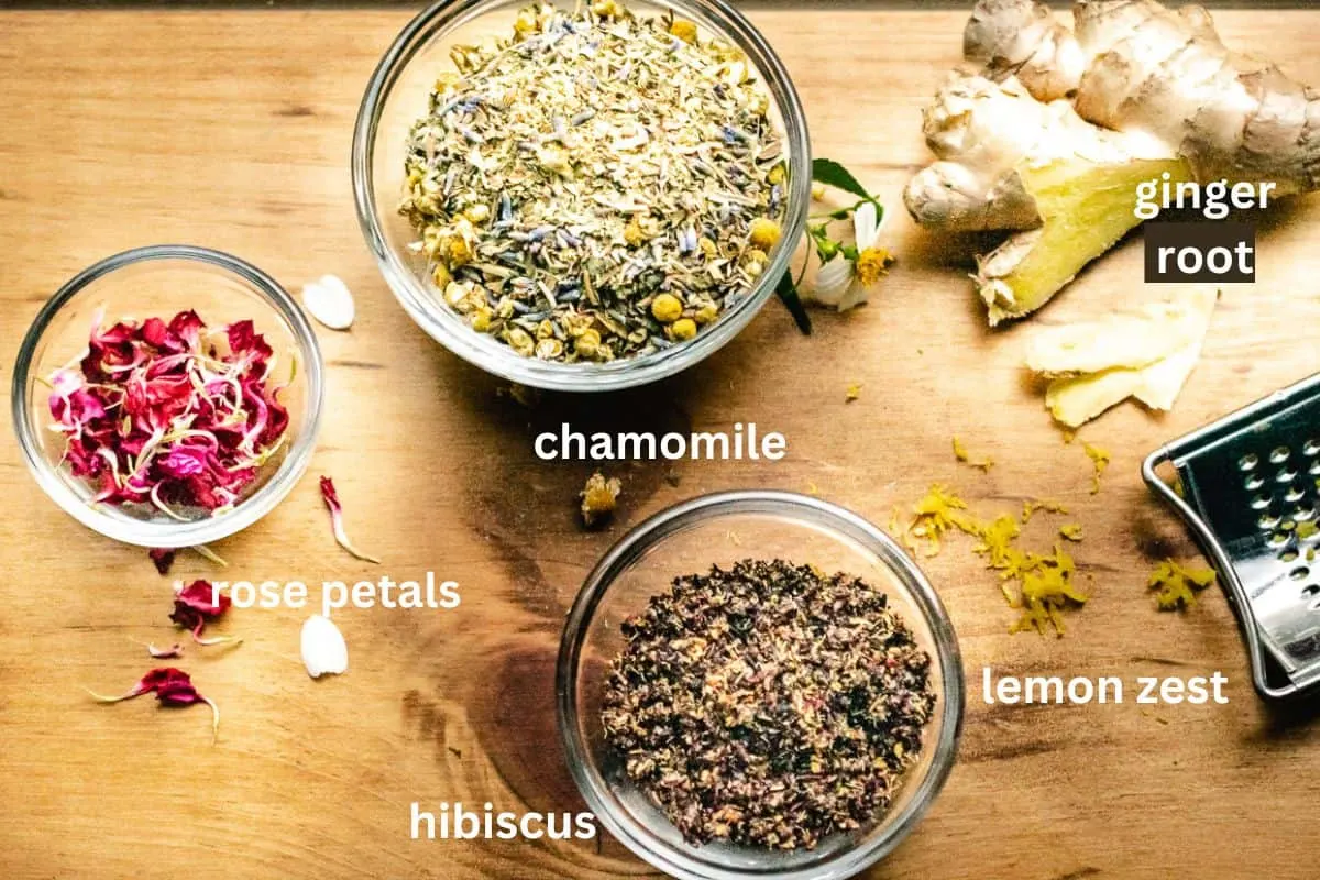 Dried chamomile, hibiscus, rose petals, lemon zest, and ginger root on a window sill.