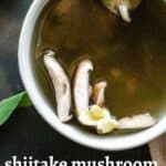 Mushroom broth in a bowl with shiitake mushroom and garlic garnish.