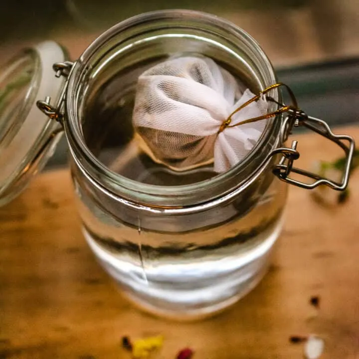 A mesh tea bag straining into a jar of water in the moonlight.