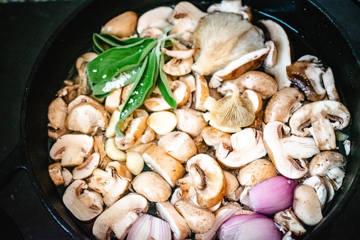 Mushrooms, sage, garlic, and shallots in a pot of water.