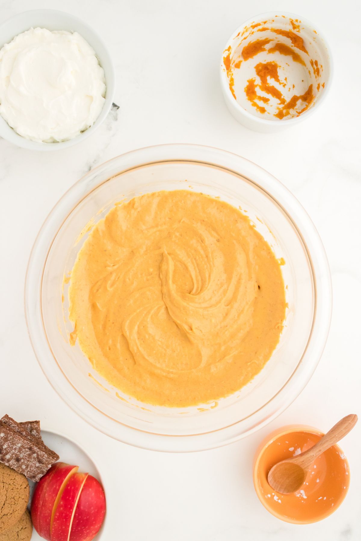 A glass mixing bowl with pumpkin, cream cheese, powdered sugar, and cinnamon mixed together.